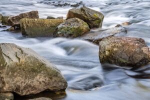 Peaceful river scene with mossy boulders and flowing water captured in long exposure.