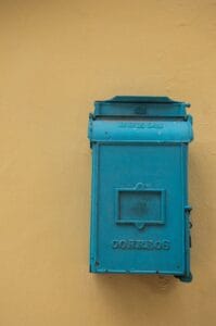 A retro blue mailbox attached to a vibrant yellow wall, perfect for vintage themes.