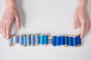 A vibrant collection of blue sewing threads arranged with hands on a white background.
