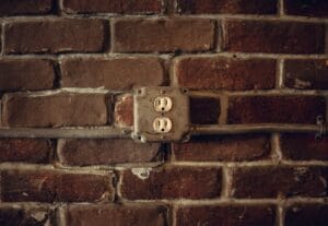 Rustic exposed brick wall featuring aged electrical sockets and metal conduit.