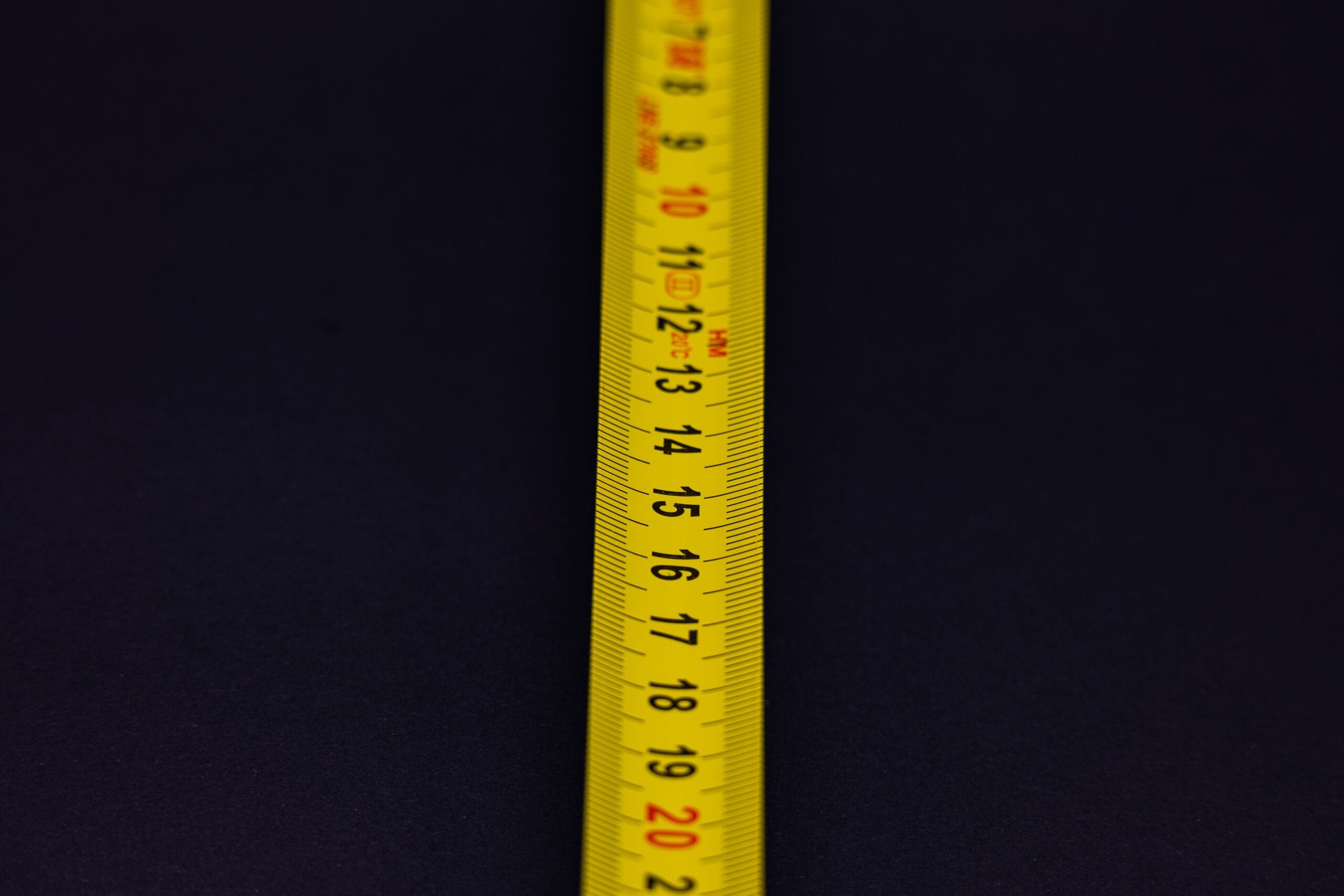 Detailed shot of a yellow measuring tape with numbers on a dark background.