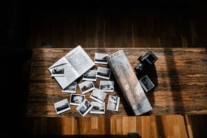 Composition of black and white photos and old travel log placed with vintage island map and obsolete photo camera on narrow wooden table